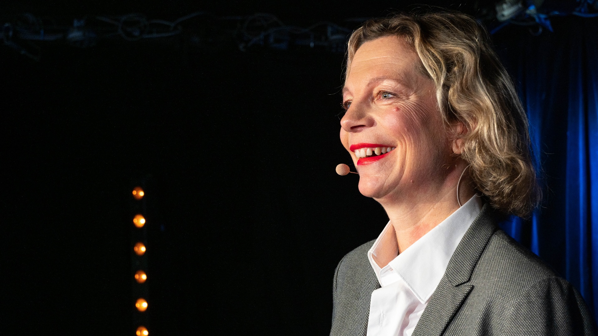 Delphine Zanelli souriante sur scène, veste grise, micro-casque, lors d'une conférence
