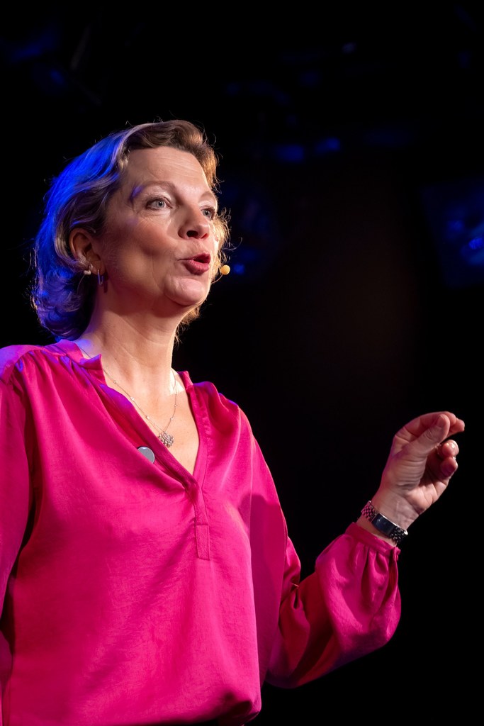 Delphine Zanelli en conférence, blouse rose, micro-casque, sur scène